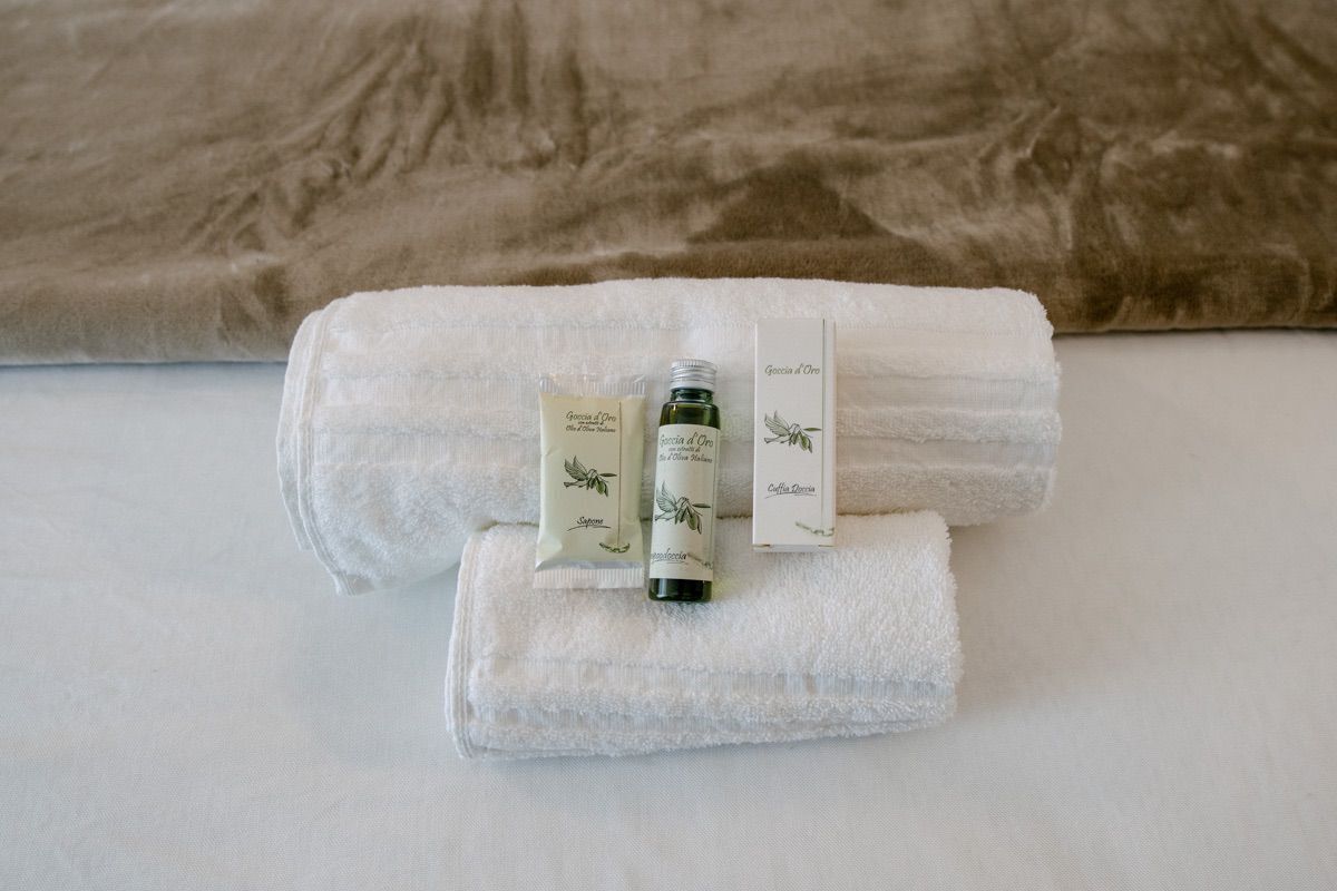 A neatly folded white towel with a bottle and a box on top, placed on a bed with a brown headboard.