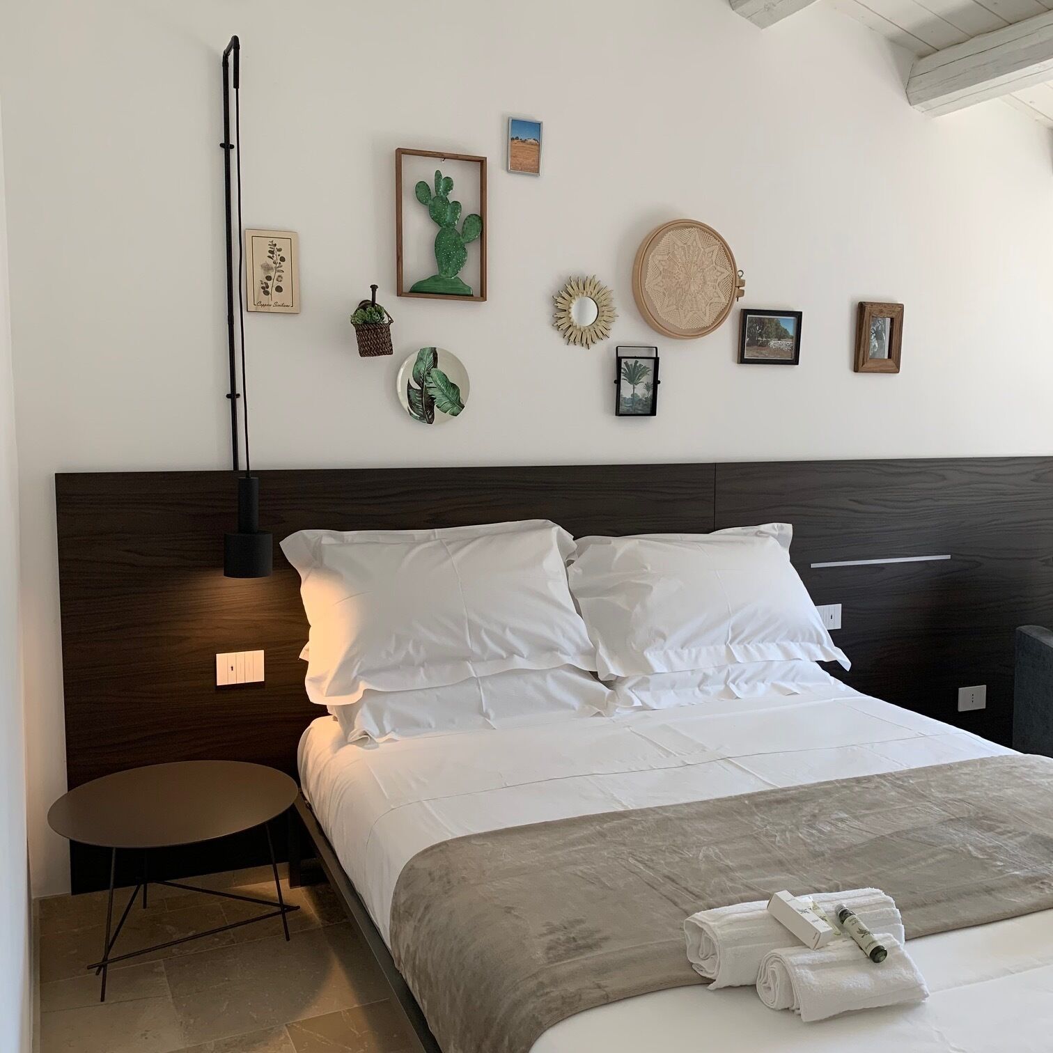 A neatly made bed with white linens, a dark wooden headboard, and a bedside table with a lamp.