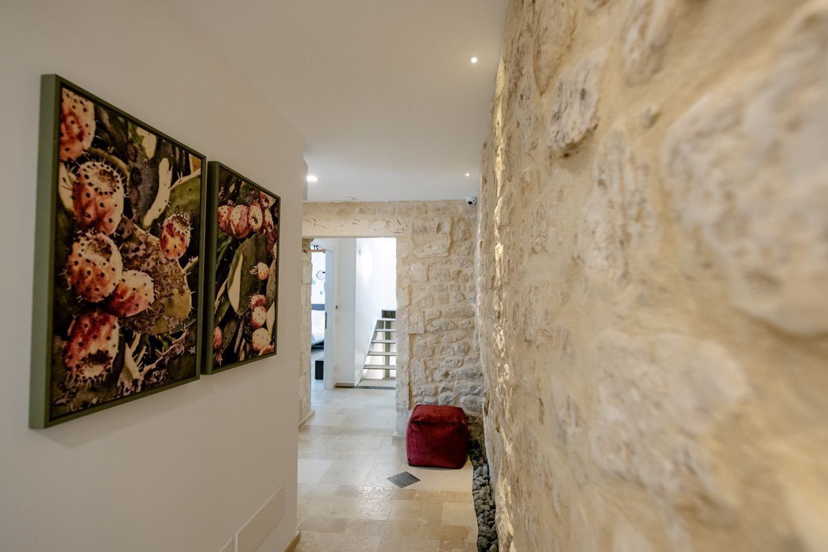 Un pasillo con pared de piedra, un reposapiés rojo y una escalera que lleva a otra habitación.