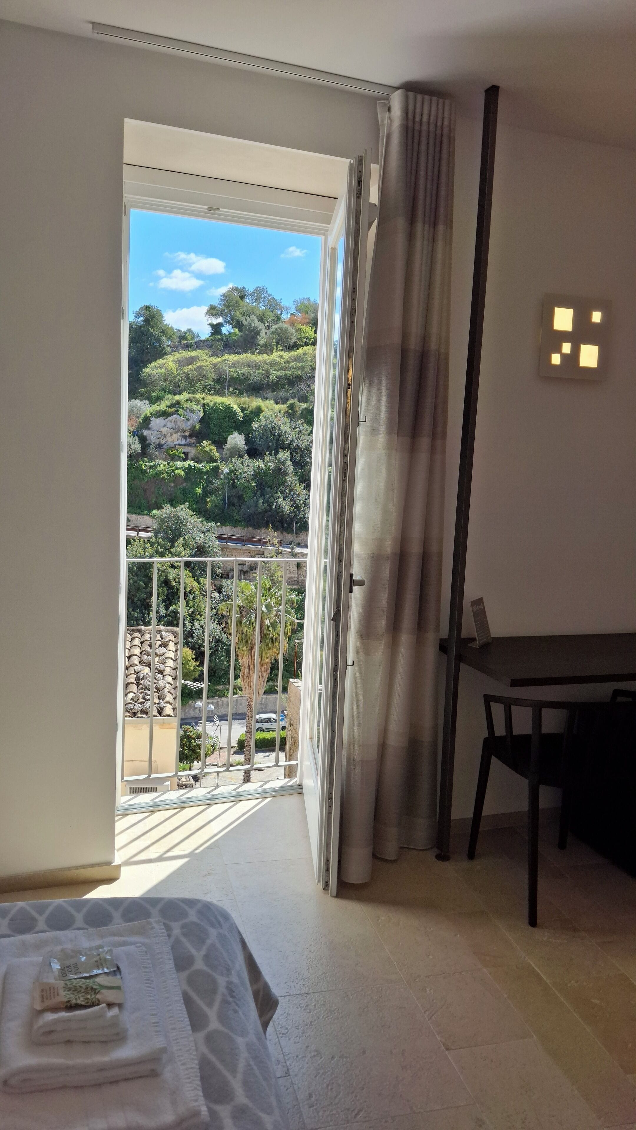A hotel room with a balcony, a bed, a table, and a chair.