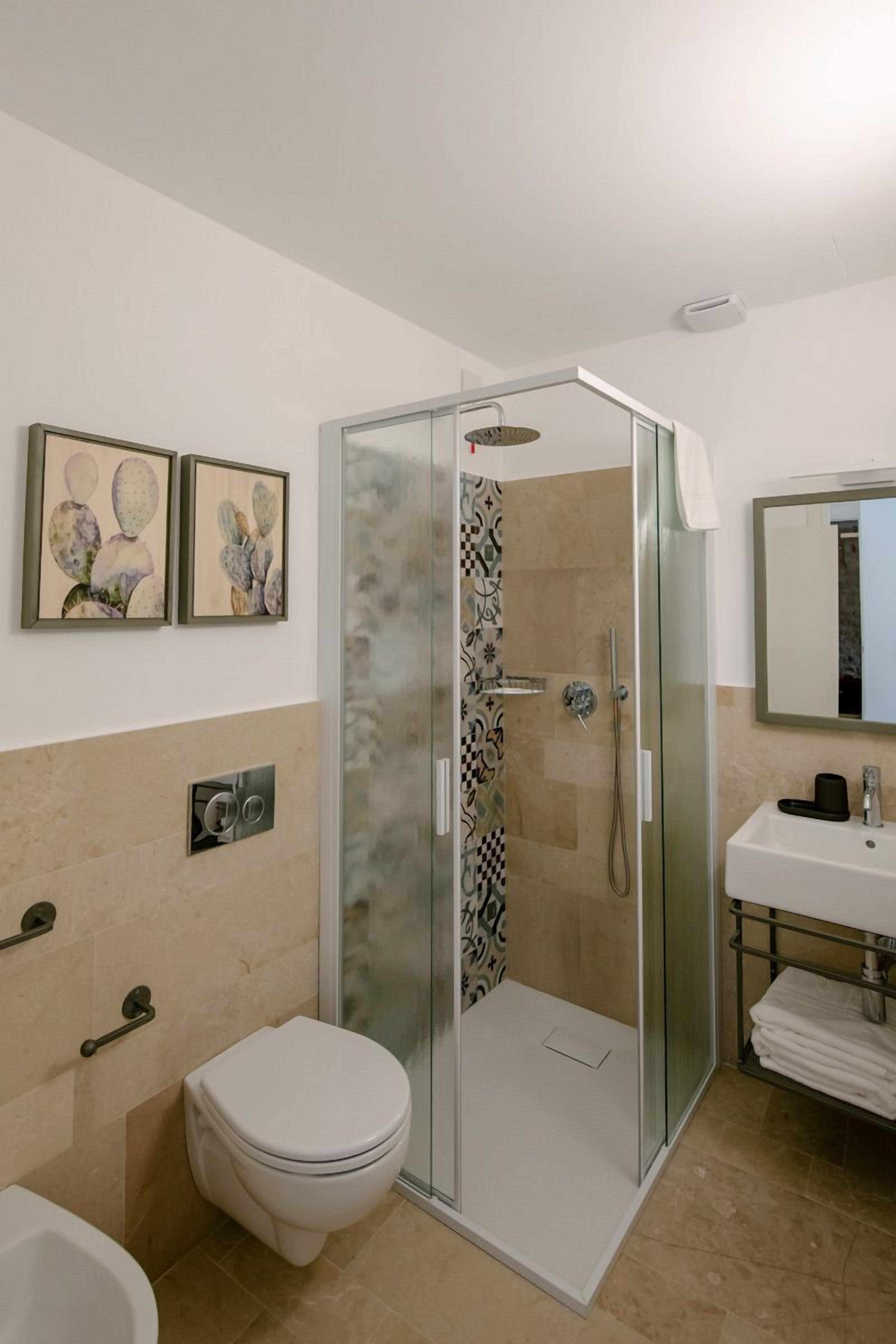 A modern bathroom with a glass-enclosed shower, a white toilet, a sink with a mirror, and two framed pictures on the wall.