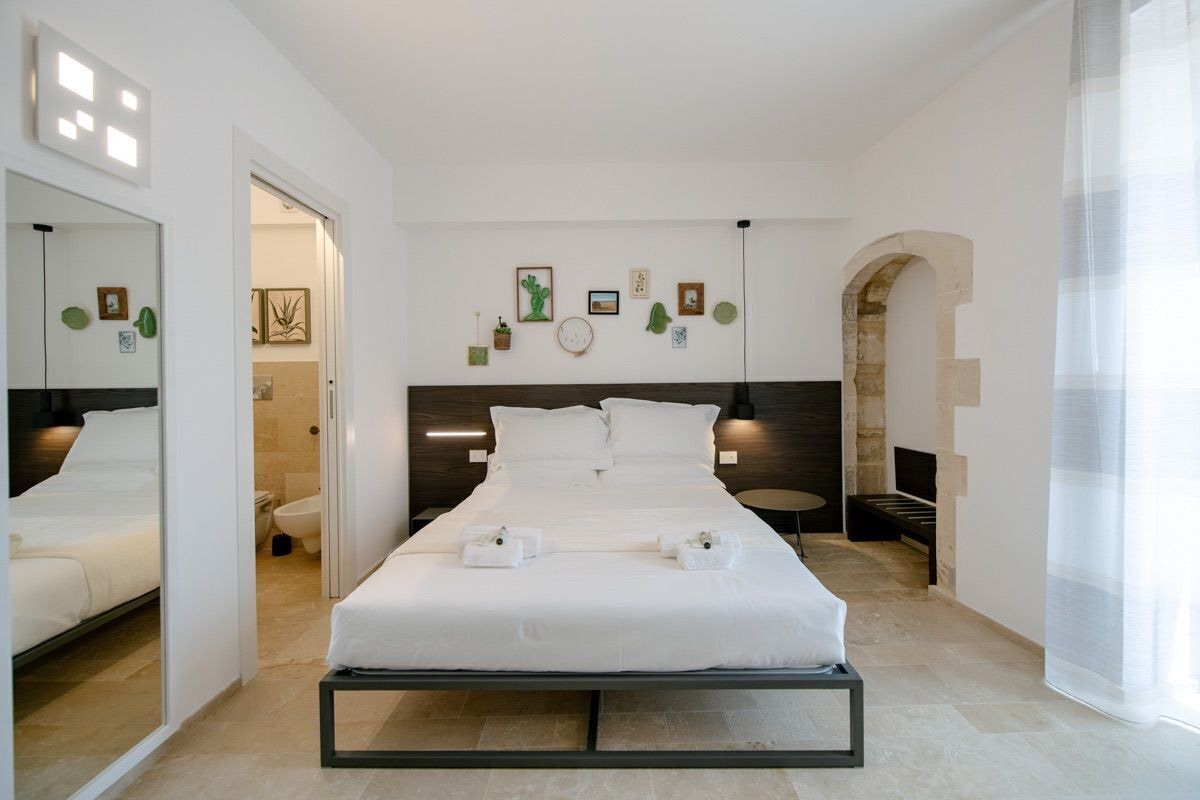 A modern hotel room with a large bed, a bathroom, and a stone archway.