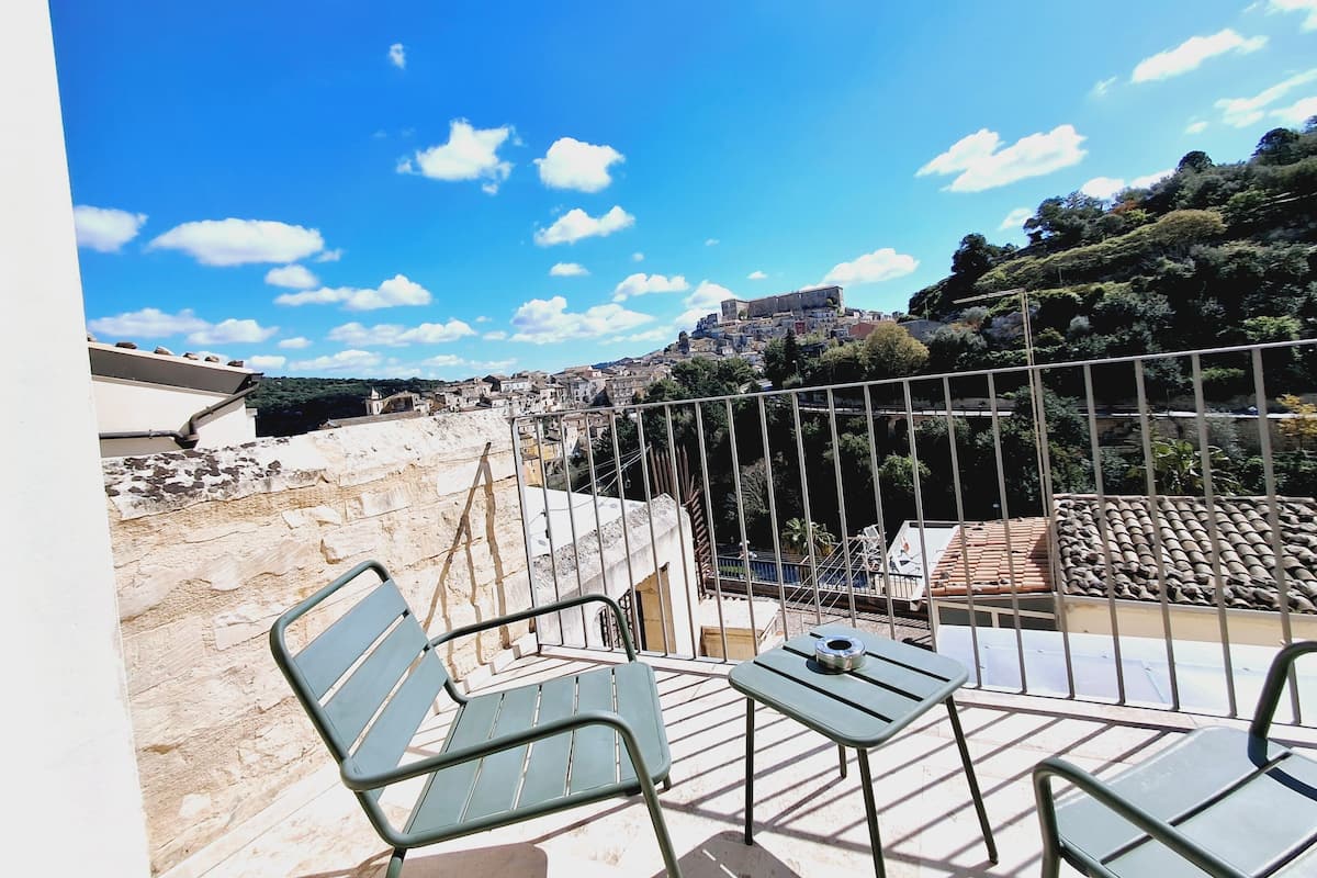 Eine Terrasse mit Blick auf eine historische Stadt, einem Metallzaun und einem Tisch mit einem Stuhl.