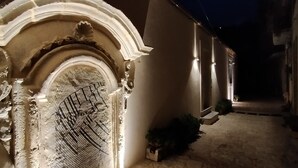 Un camino de piedra conduce a un edificio con una entrada ornamentada y apliques de luz iluminados.