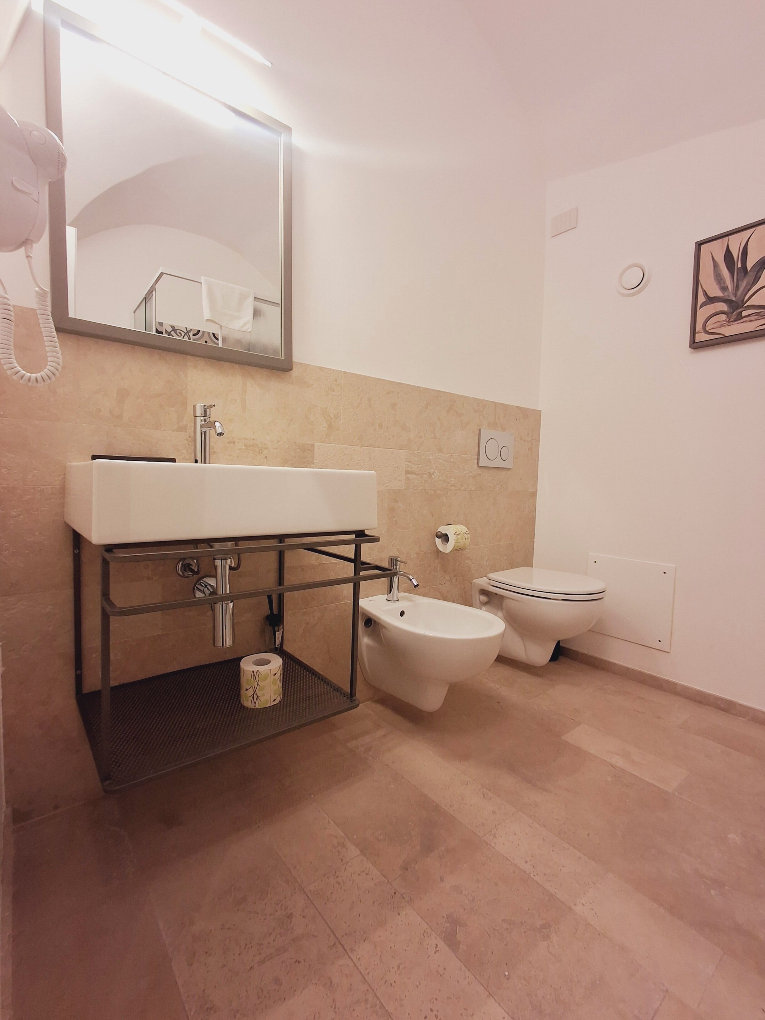 A modern bathroom with a white sink, bidet, and toilet. There is a towel rack and a mirror above the sink.
