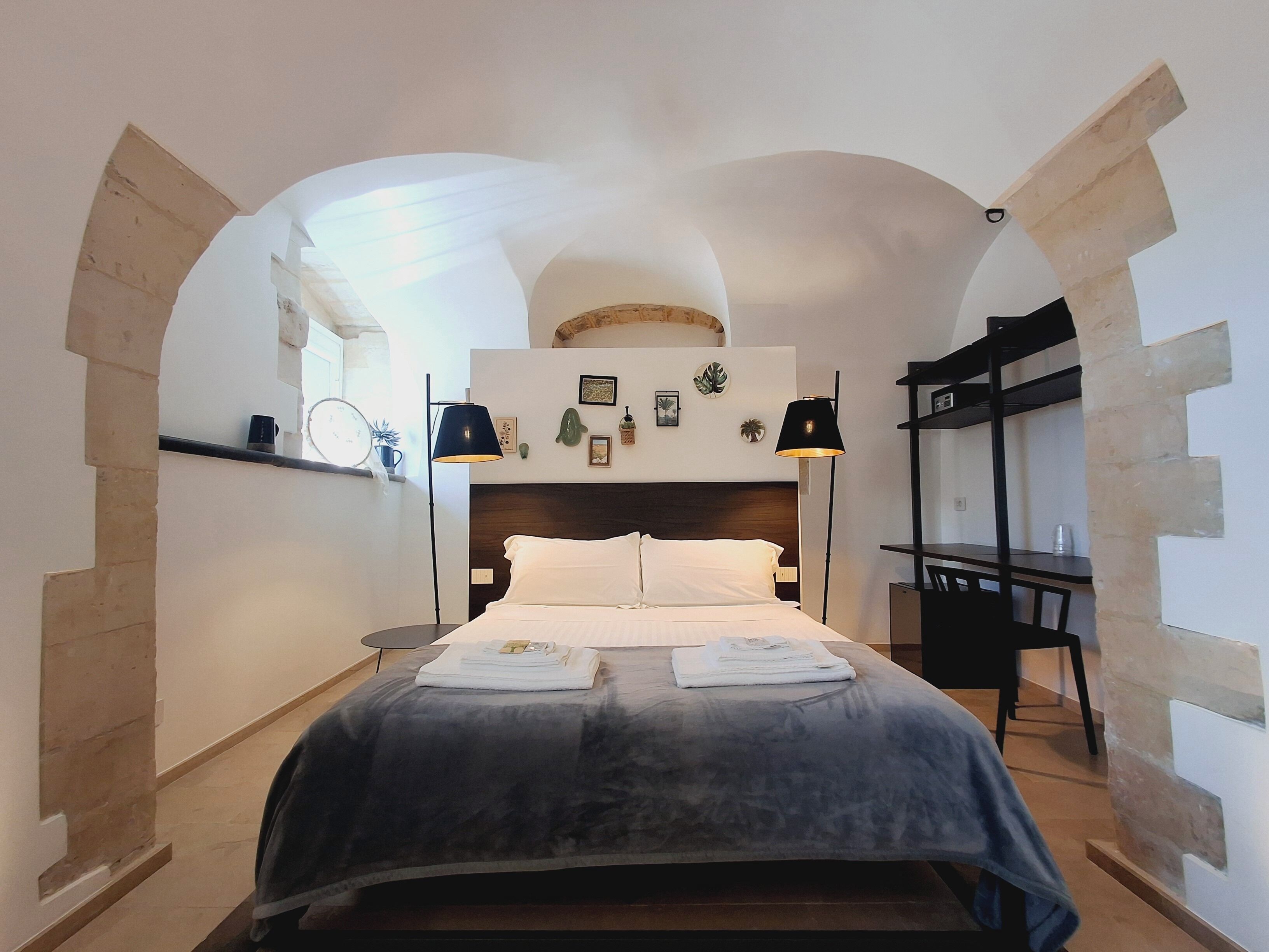 A bedroom with a bed, two bedside lamps, a wooden headboard, and a small desk with a chair.