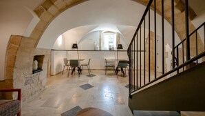 Una habitación amplia con un arco de piedra, una escalera con barandilla metálica y un área de comedor con sillas y mesas.