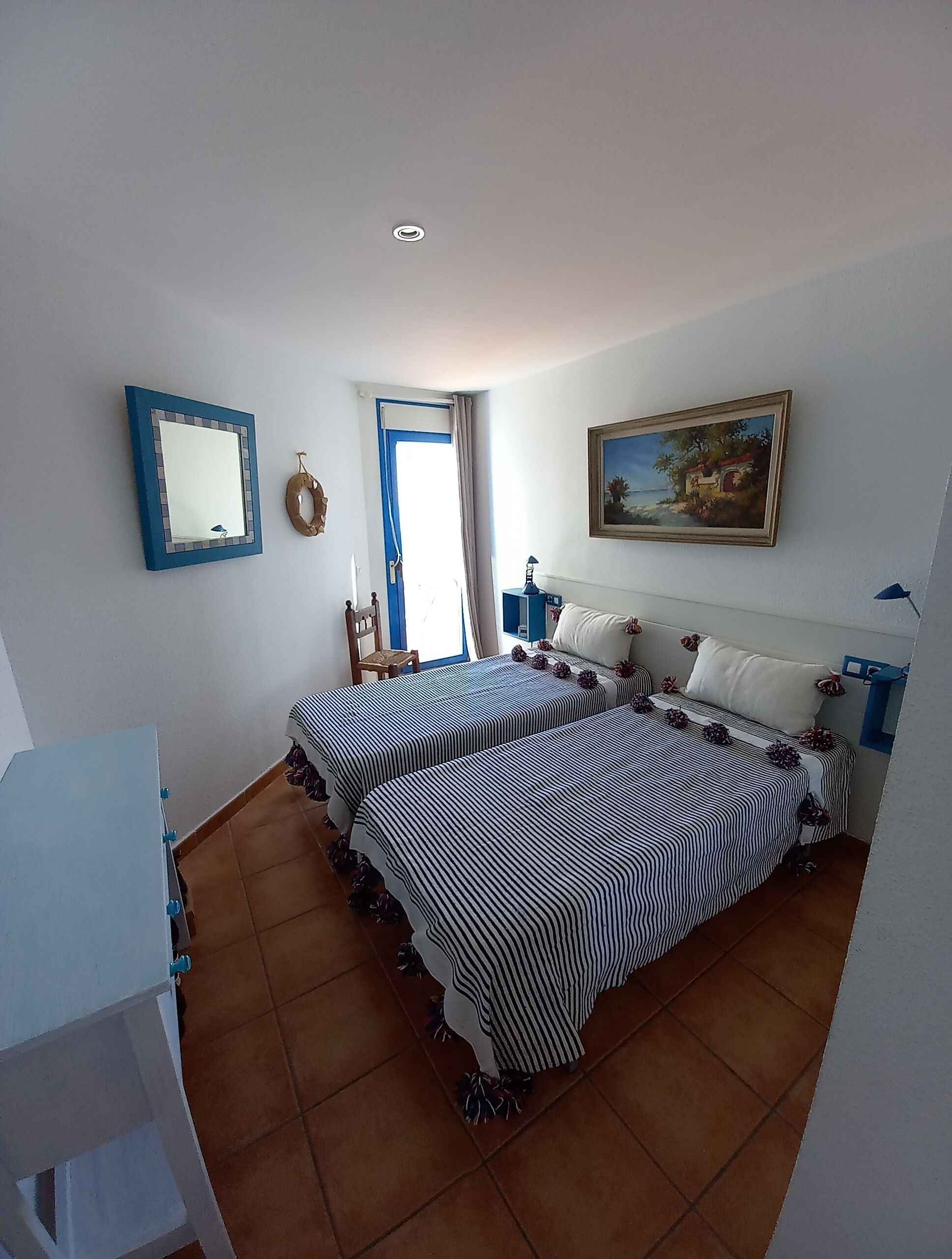 A bedroom with two beds, a painting, a mirror, and a door.