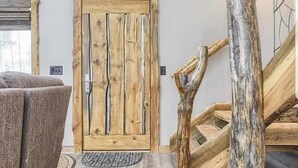A rustic interior with a wooden door, a staircase with a natural wood finish, and a textured rug on the floor.