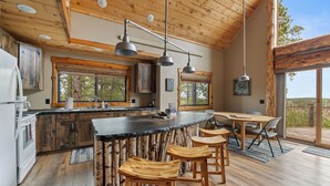 A rustic kitchen with wooden bar stools, a large island, and a dining table with chairs.