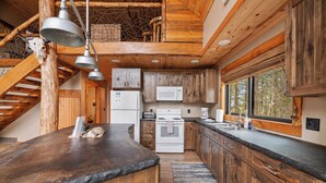 A rustic kitchen with wooden cabinets, a stone countertop, and a large window.