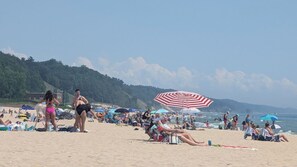 A crowded beach with people sunbathing and swimming, umbrellas, and a hilly landscape in the background.
