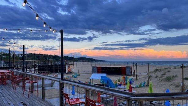 A beachside deck with red chairs and umbrellas, overlooking a sandy beach and ocean.