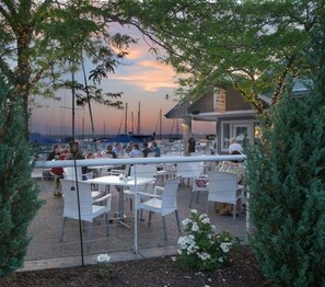 An outdoor seating area with tables and chairs, overlooking a marina with boats.