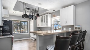 Une cuisine moderne dotée d’un îlot central, de tabourets de bar et de casseroles suspendues.
