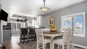 A modern kitchen with a dining area, large windows, and a view of the outdoors.