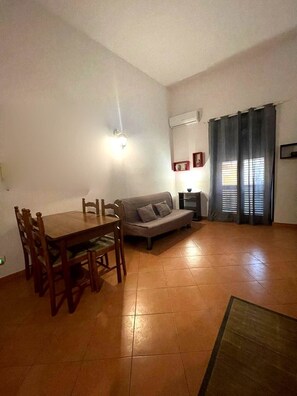 Ein Wohnzimmer mit einer Couch, einem Esstisch mit Stühlen, einer Klimaanlage und einem Fenster mit Vorhängen.