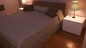 A neatly made bed with a headboard, two bedside tables with lamps, and a tiled floor. - Hola Cathedral House (Palermo)