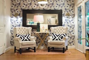 Une pièce comprenant deux fauteuils rembourrés avec des coussins à motifs noir et blanc, une petite table avec une lampe et un miroir décoratif au-dessus.