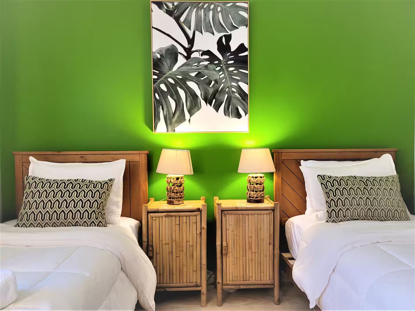 A room with two beds, green walls, and a framed artwork above the beds.