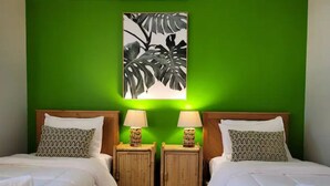 A hotel room with two beds, green walls, and a tropical leaf painting above the beds.
