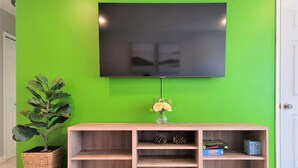 A room with a green wall, a mounted TV, a wooden console table with shelves, and a potted plant.