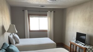 Une chambre avec deux lits, un bureau avec un ordinateur, une lampe et une fenêtre avec des rideaux.
