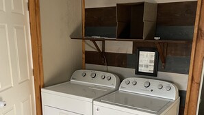 Une buanderie équipée de deux machines à laver et de deux sèche-linge à chargement frontal superposés, avec des étagères en bois au-dessus, et une porte sur le côté gauche.