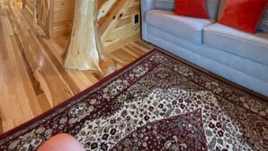 Een houten interieur met een trap, een bank met rode kussens en een kamerbreed tapijt met een patroon.