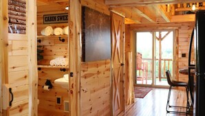 Interieur van een chalet met houten wanden, een plafondlamp, een badkamer met toilet en wastafel, en een eethoek met een tafel en stoelen.
