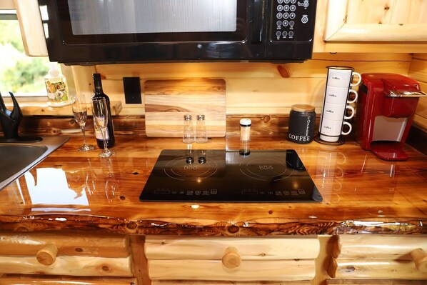 Una cocina con un fogón de inducción negro, un microondas, una cafetera y una botella de vino.