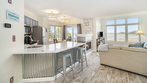 A modern kitchen with a central island, bar stools, a fireplace, and a view of the beach. - Updated, LK MI View - Pet Friendly! (Manistee)