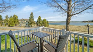 A deck with a table and chairs overlooking a lake and a house. - Updated, LK MI View - Pet Friendly! (Manistee)