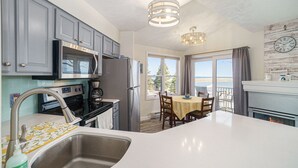 A kitchen with grey cabinets, stainless steel appliances, a white countertop, and a dining area with a table and chairs. - Updated, LK MI View - Pet Friendly! (Manistee)