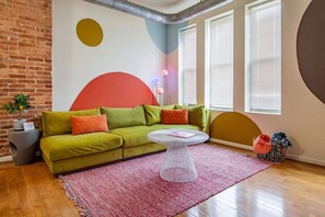 A modern living room with a green sofa, a round coffee table, and a red rug. - Colorful & Quirky 2-BR Loft w/Private Deck | MICA, JH & UMMC (Baltimore)