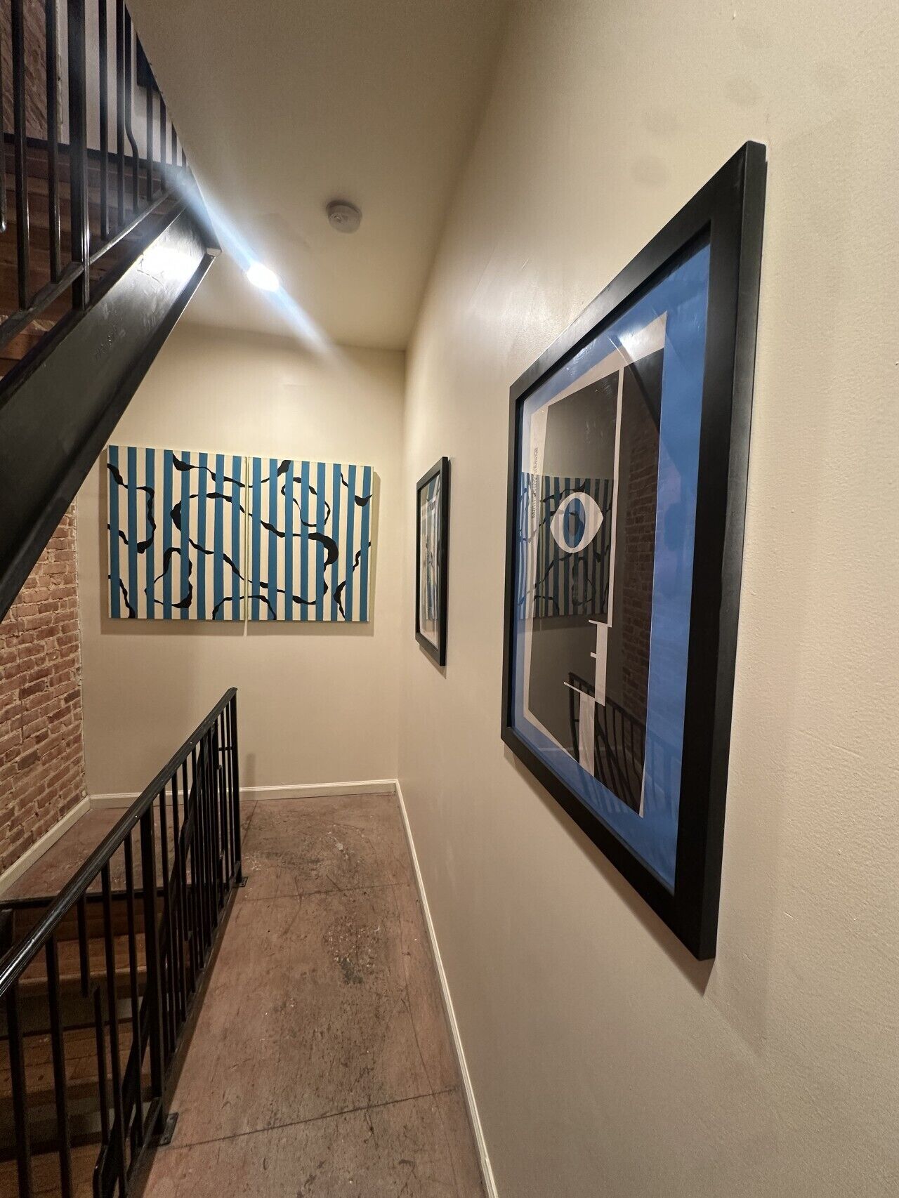 Un pasillo con una escalera, un muro de ladrillo y obras de arte en las paredes.