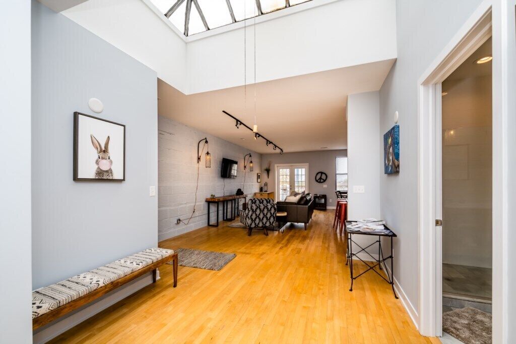 A spacious living area with a high ceiling, wooden flooring, a bench, a sofa, and a table.