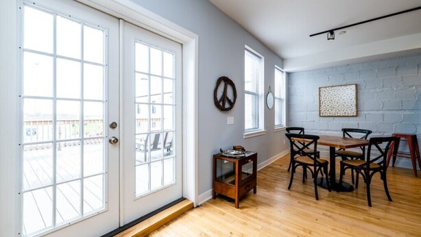 Una habitación amplia con ventanas grandes, suelo de madera, una mesa de comedor con sillas y un símbolo de la paz colgado en la pared.