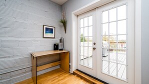 Una habitación con pared de ladrillo blanco, un escritorio de madera, un cuadro enmarcado y un ventanal con vistas al exterior.