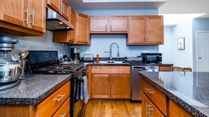 Una cocina moderna con armarios de madera, encimeras de granito, estufa a gas, microondas y pileta.