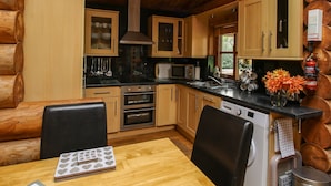 A cozy log cabin kitchen with wooden cabinets, a dining table, and a microwave. - Brynallt Country Park (Ellesmere)