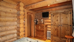 A log cabin bedroom with a wooden bed, dresser, and wardrobe, a radiator, and a television mounted on the wall. - Brynallt Country Park (Ellesmere)