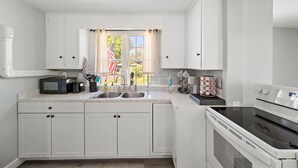 Een moderne keuken met witte kasten, een dubbele spoelbak, een magnetron, een fornuis en een raam met gordijnen.