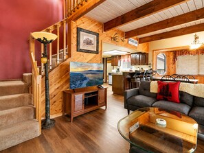 L’intérieur chaleureux d’un chalet avec un escalier en bois, une télévision, un canapé et un coin repas.