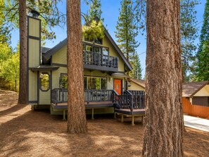 Un chalet à deux étages doté d’un balcon, entouré de grands arbres.