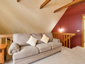 Un canapé beige agrémenté de deux coussins, dans une pièce dont un mur est peint en rouge et qui possède un escalier en bois.