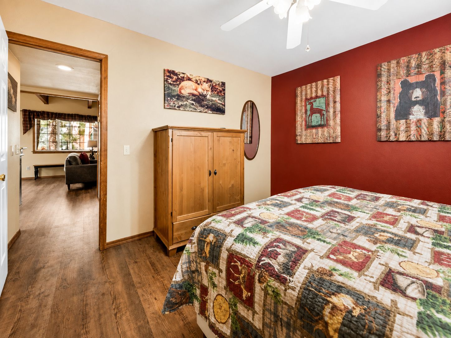A bedroom with a quilted bedspread, wooden wardrobe, and two wall-mounted paintings.