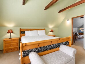 Une chambre à coucher avec un lit en bois, deux tables de chevet, une commode, un banc et un téléviseur placé dans un coin.