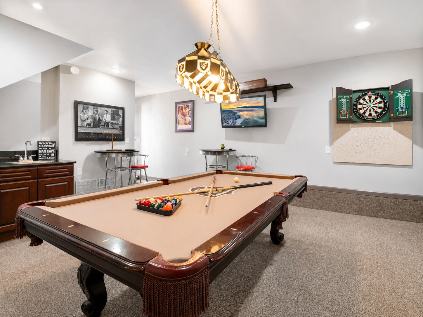 Une table de billard avec une queue de billard, un jeu de fléchettes et un tableau encadré accroché au mur.