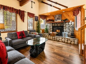 Un salón acogedor con chimenea de piedra, un sofá con una manta roja y una mesa de centro de vidrio.